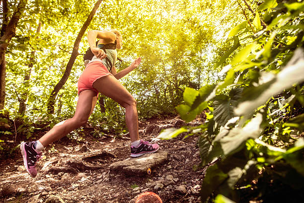 Side view of a woman running uphill in a forest Side view shot of a sports woman running uphill on rough terrain in a forest. cross country running stock pictures, royalty-free photos & images