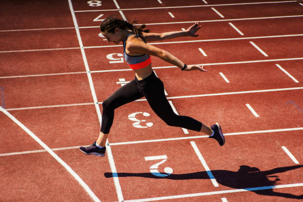 Side view of female teen athlete in sports bra and tights successfully finishing race on track at stadium Side view of female teen athlete in sports bra and tights successfully finishing race on track at stadium athleticism stock pictures, royalty-free photos & images