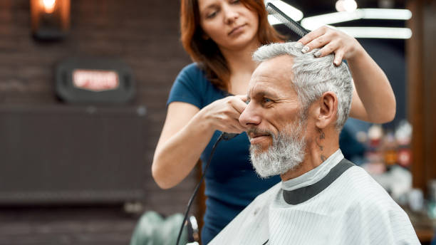 Side view of happy handsome bearded man getting haircut at barbershop. Young barber girl working with hair clipper Side view of happy handsome bearded man getting haircut at barbershop. Young barber girl working with hair clipper. Barbershop. Beauty salon. Barber tools. Mens haircut cutting hair stock pictures, royalty-free photos & images