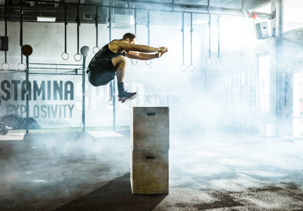 Side view of male athlete jumping on crate during sport training in a gym. Athletic man jumping on a crate while having sports training in a gym. cross training stock pictures, royalty-free photos & images