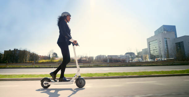 zijaanzicht van rijpe vrouw die elektrische duwscooter in stad berijdt - elektrische step stockfoto's en -beelden