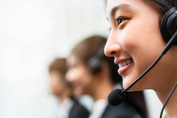 Side view of smiling woman consultant wearing microphone headset of customer support phone operator at workplace. stock photo
