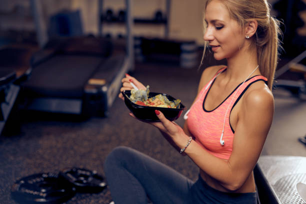 Side view of woman eating healthy food in gym. stock photo