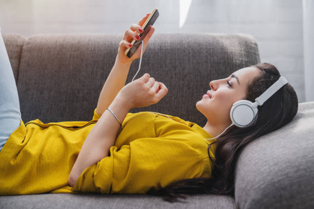 tampilan samping wanita muda mendengarkan musik online di smartphone di headphone - musik subjek potret stok, foto, & gambar bebas royalti