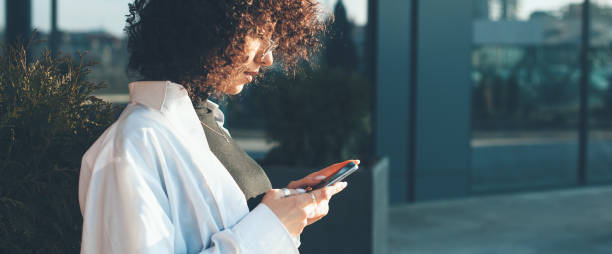 Side view photo of a curly haired woman chatting on mobile with friends stock photo