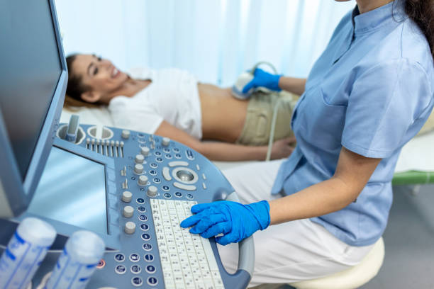 Side view portraits of gynecologist in sterile gloves using ultrasound scanner while examining female patient. woman lying on daybed on blurred background stock photo