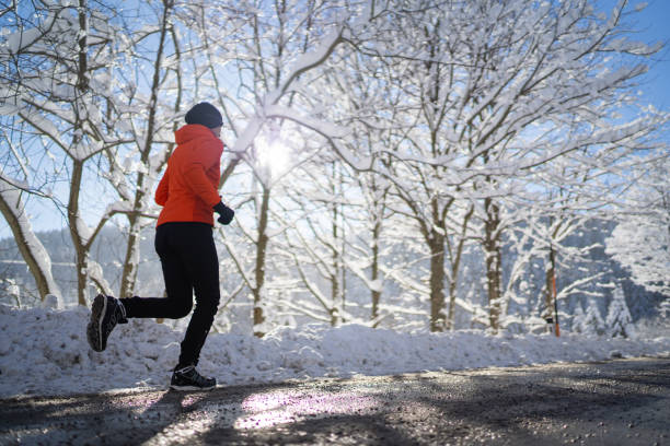 side view woman jogging running on road cold sunny winter day stock photo