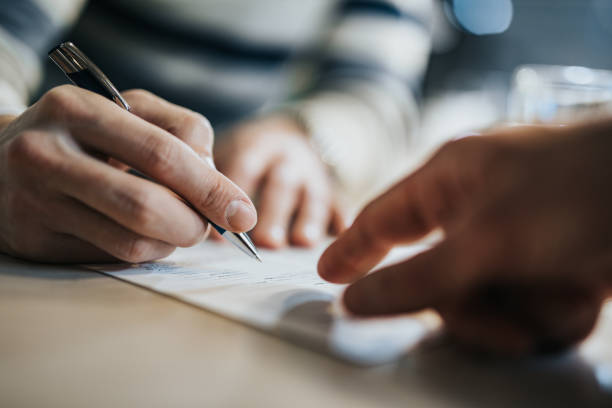 Close up of unrecognizable man signing a contract while financial advisor is aiming at the place he need to sign.