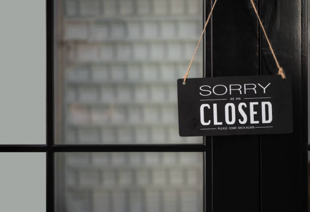 Signboard of tell sorry we are closed business and please come back again when situation improved with hanging to door front at shop. stock photo
