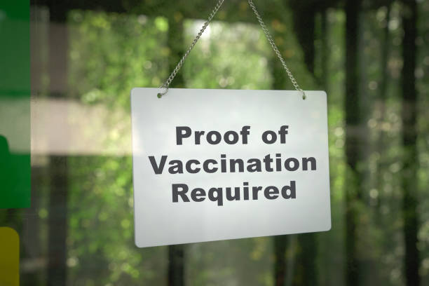 Signboard, Proof of Vaccination Required hanging on the door front of a shop. stock photo
