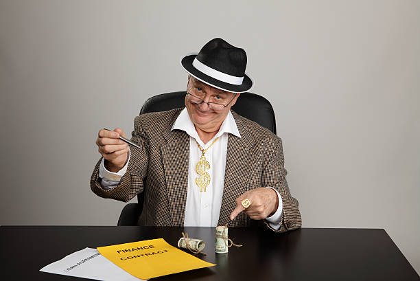 Sign-up for the money Dodgy-looking man holding a pen and pointing to rolls of money on the desk in front of him. signup stock pictures, royalty-free photos & images
