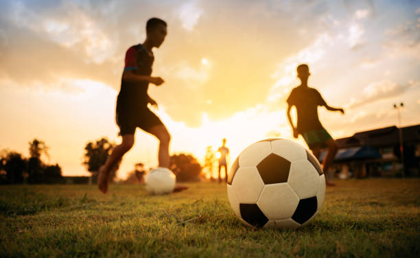 siluett action sport utomhus av en grupp barn ha kul att spela fotboll fotboll för motion i gemenskapens landsbygdsområde under skymningen solnedgången himlen. - barndom bildbanksfoton och bilder