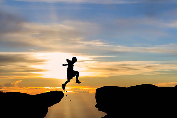Silhouette of a child jumping cliff with sunset background stock photo