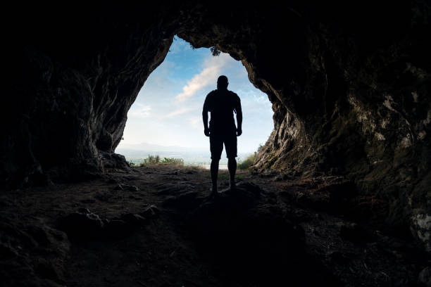 Silhouette of a male person at the cave entrance Silhouette of a male person at the cave entrance cave stock pictures, royalty-free photos & images