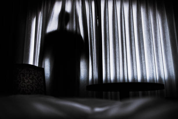 Silhouette of a man hinding behind a curtain stock photo