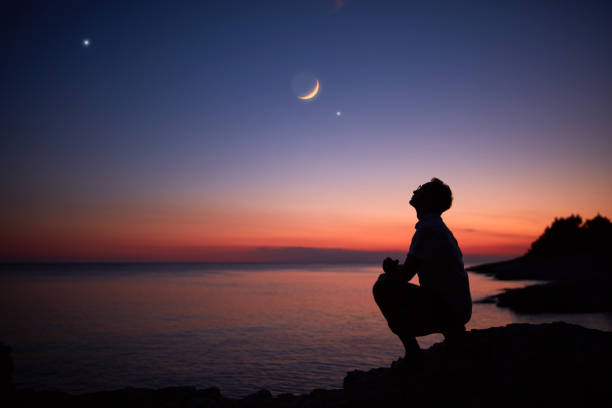 Silhouette of a man looking at the Moon and stars over sea ocean horizon. stock photo