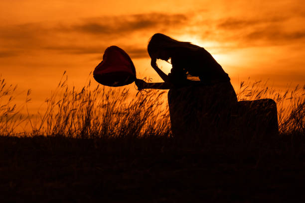 Silhouette of a sad woman sitting on suitcase with heart shaped balloon Silhouette of a sad woman sitting on suitcase with heart shaped balloon  at the sunset. broken suitcase stock pictures, royalty-free photos & images