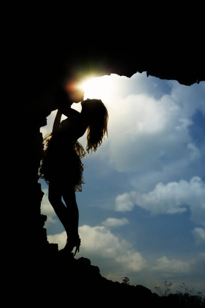 Silhouette of a woman standing in the dark cave against a cloudy sky and an evening sun stock photo