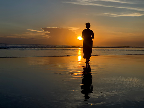 Silhouette of the person in the beach at sunset. A Woman walking alone toward the sun. Fragility concept. Strength and close to the light concepts on beach nature landscape background.