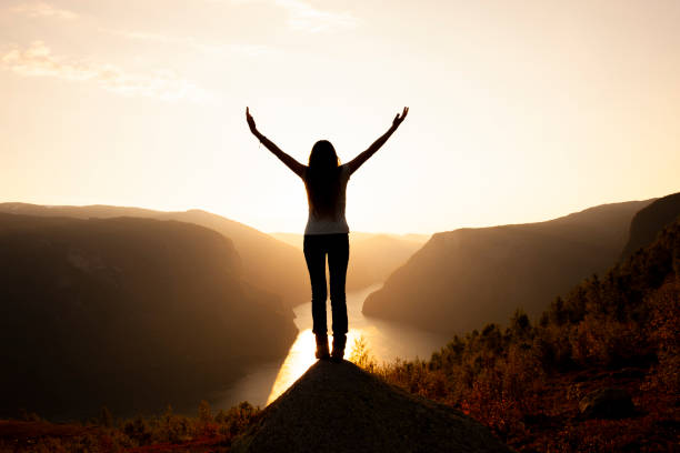 Silhouette of a woman with arms outstretched at sunrise Silhouette of a woman with arms outstretched at sunrise on a mountain top empowered stock pictures, royalty-free photos & images