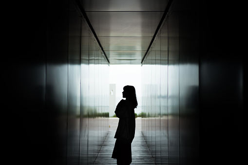 Silhouette of Asian woman standing against dark corridor in a park.