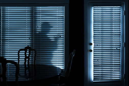 This photo illustrates a silhouette  of a burglar or thief sneeking up to back door at night. View from inside the residence.