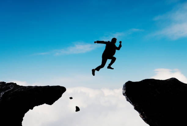 Silhouette of businessman jumping over the cliff stock photo