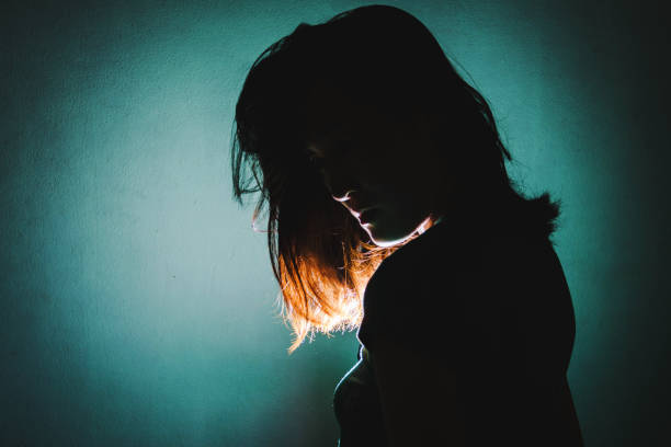 silhouette of depress woman standing in the dark with light shine behind stock photo