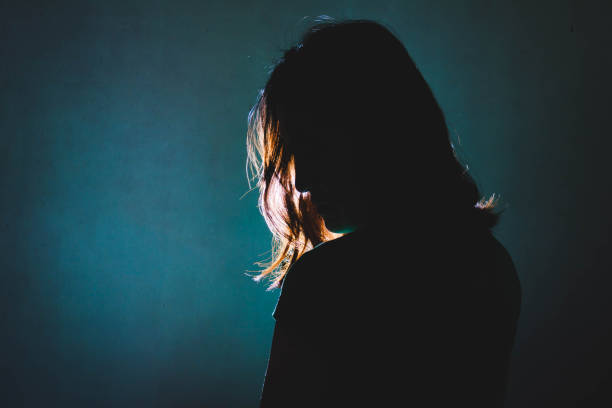 silhouette of depress woman standing in the dark with light shine behind stock photo
