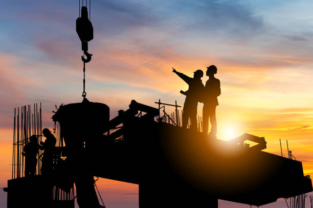 Silhouette of Engineer and worker checking project at building site background, construction site at sunset in evening time. stock photo