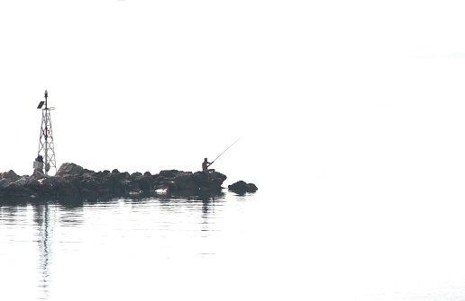 Silhouette of fisherman with fishing rods and lighthouse on the pier. Minimalism.
