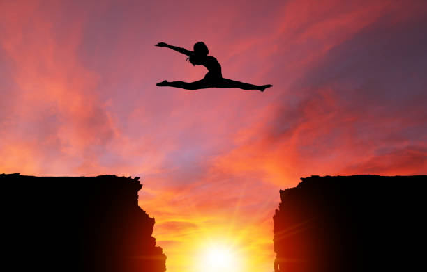 Silhouette of Girl Leaping Over Cliffs With Sunset Landscape Silhouette of girl dancer in a split leap over dangerous cliffs with dramatic sunset or sunrise background and copy space. Concept of faith, conquering adversity, taking risk; challenge, courage, determination or achievement.  Please note the sunset background was shot in Calgary on 10-24-2017 (reference image attached).  The dancer model was shot in studio on 04-07-2016 (Reference image attached and Model Release also attached). The dance model was isolated in Photoshop and then composited onto the sunset background as a silhouette. doing the splits stock pictures, royalty-free photos & images