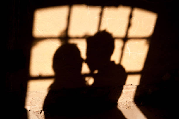 silhouette di amanti alla finestra. ombre di una coppia innamorata sul muro. silhouette degli sposi sul muro. - couple kiss foto e immagini stock