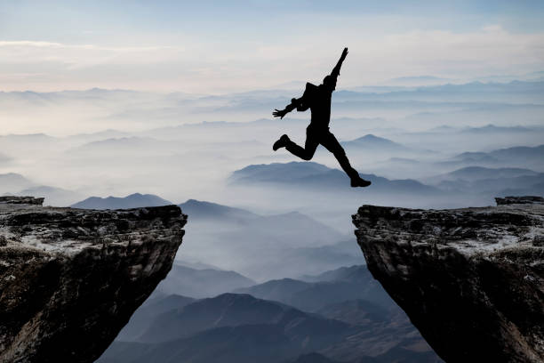 Silhouette of man jumping from one cliff to another cliff with excitement stock photo
