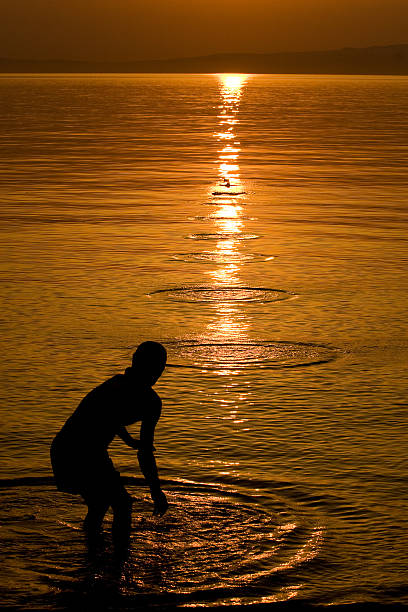Silhouette of Man Skipping Stones in Sea stock photo