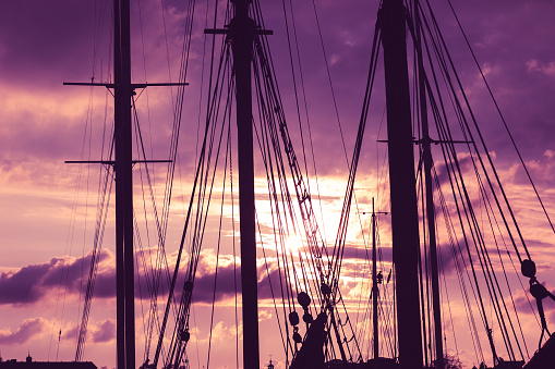 Silhouette of masts and ropes of a wooden old sailing ship against the background of the evening dark pink purple neon magical sky