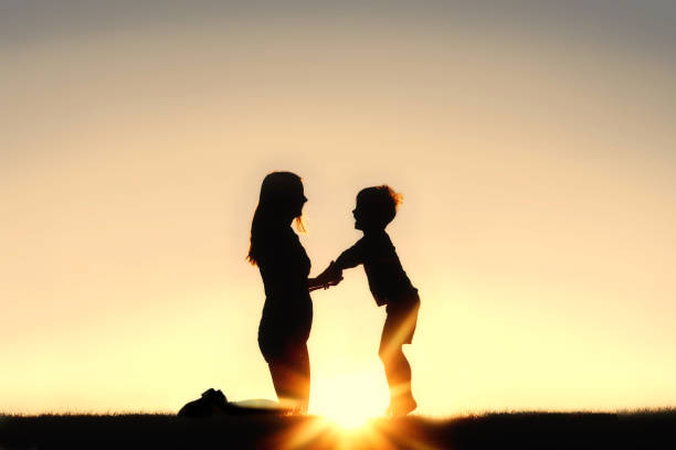 Silhouette of Mother and Young Child Holding Hands at Sunset stock photo
