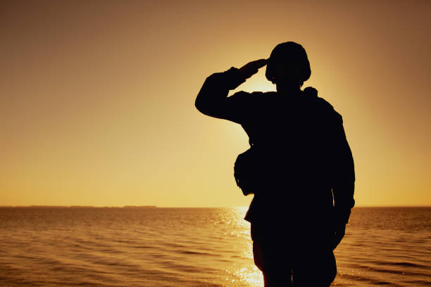 Silhouette of soldier salutes on sunset background stock photo