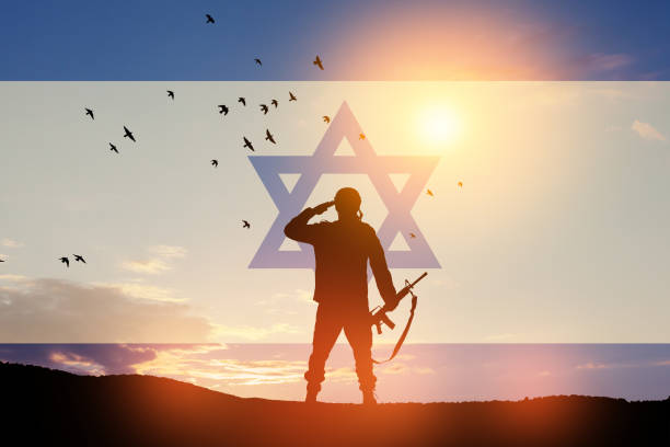 Silhouette of soldier saluting against the sunrise in the desert and Israel flag. stock photo