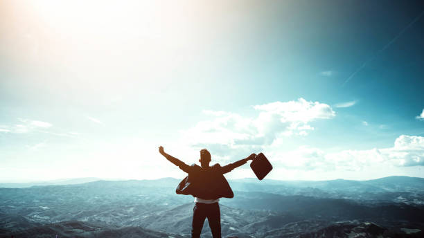 Silhouette of successful businessman keeping hands up hiking on the top of mountain - Celebrating success, winner and leader concept stock photo