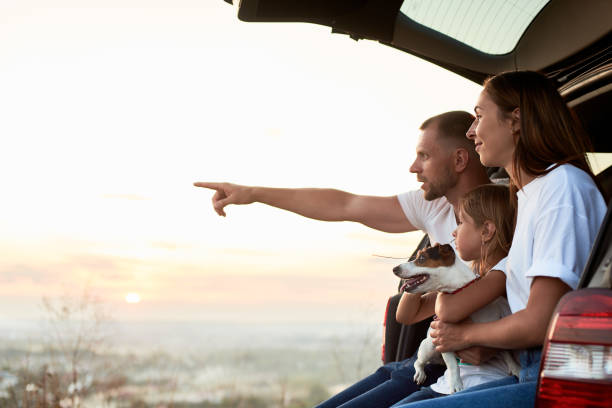 Silhouette of the family in a car trunk on the sunset Side view of the family sitting in the car trunk outside the city, watching the sunset, father is pointing on the horizon, copy space road trip stock pictures, royalty-free photos & images