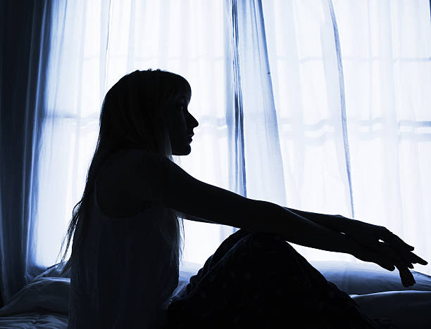 Silhouette of woman sitting in bed by window stock photo