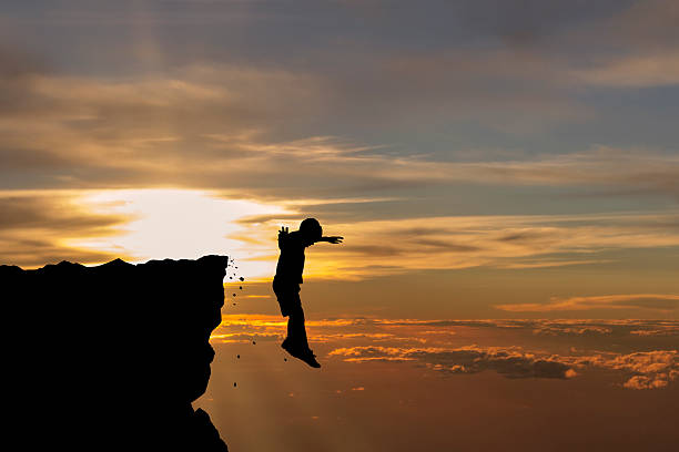 Silhouette of young man falling off a cliff stock photo