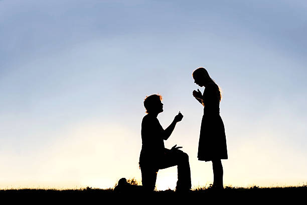 Silhouette of Young Man with Engagement Ring Proposing to Woman A silhouette of a young man, down on one knee and holding a diamond engagement ring, proposing to his girlfriend. fiancé stock pictures, royalty-free photos & images