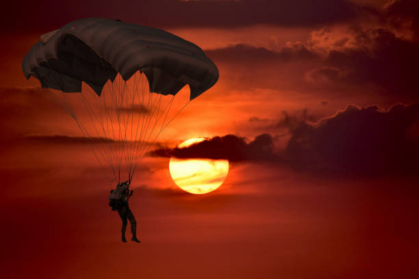 Silhouette skydiver control with  parachute Silhouette skydiver control with  parachute in sunset  sky background with dark cloudy parachuting stock pictures, royalty-free photos & images
