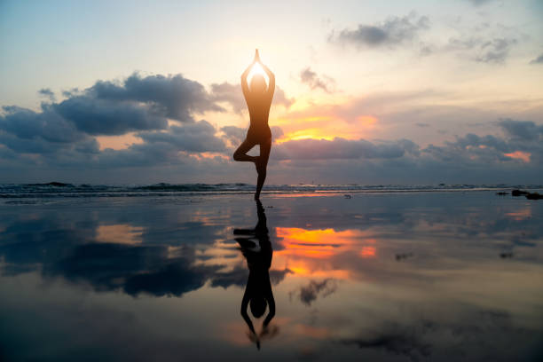Silhouette young woman practicing yoga on the beach . stock photo