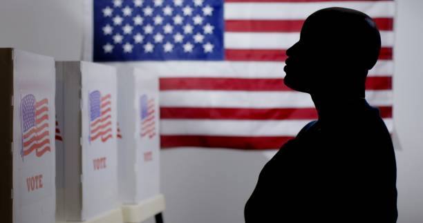 Silhouetted African American man with hand on heart at voting booths MS silhouetted African American man looking at voting booths, with hand over heart, US flag on wall behind voting booth stock pictures, royalty-free photos & images
