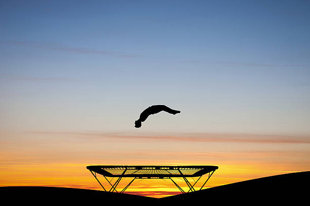 silhouetted ginnasta a pedana elastica per saltare al tramonto - tappeto elastico foto e immagini stock