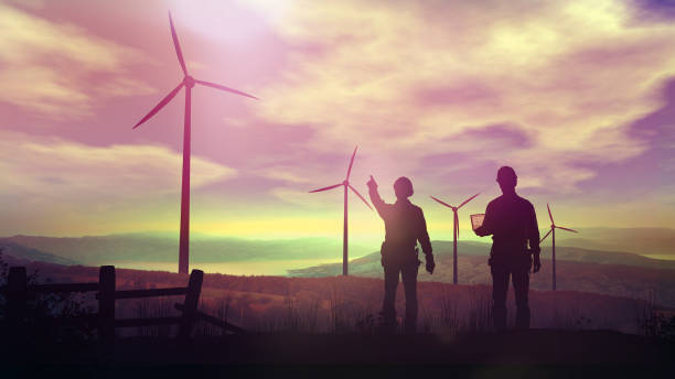 Silhouettes of engineers watching wind farms at sunset. stock photo