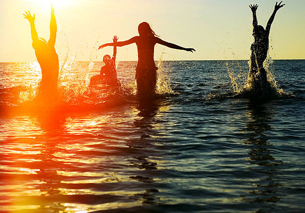 Silhouettes of people jumping in ocean stock photo